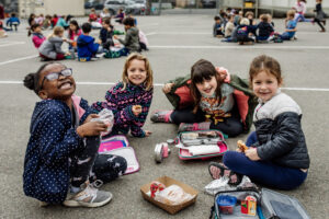 Smiling kids on the playground eating lunch, photo by Sara Pietras